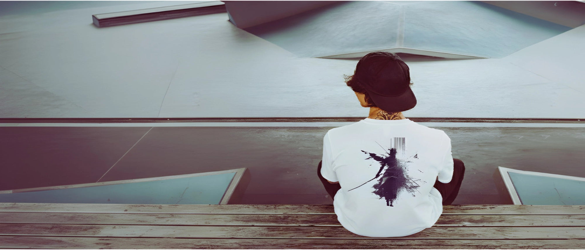 Person sitting on a bench with a white shirt featuring a black design, looking at a large screen.